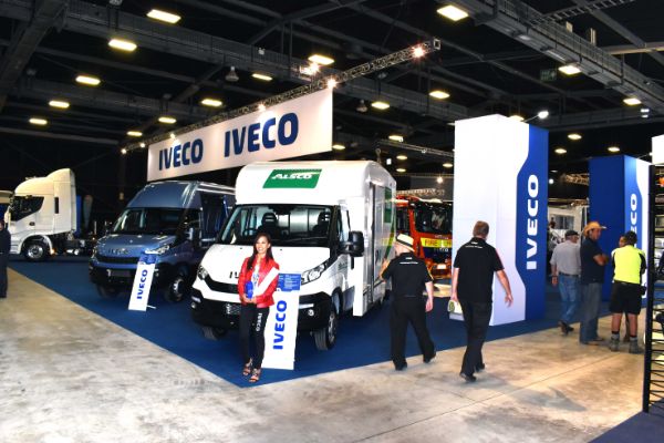 Thumbnail - A wide shot of the Iveco exhibition area with trucks on display and people walking around.